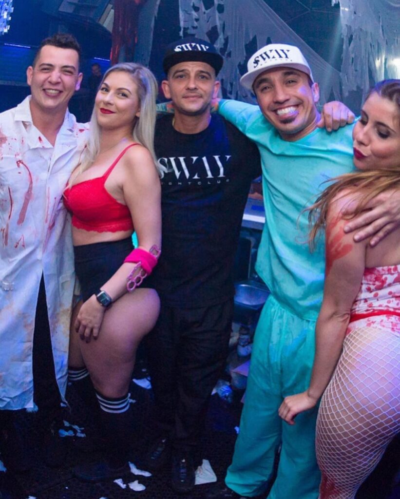 Five adults in Halloween costumes posing together in a dark party setting.