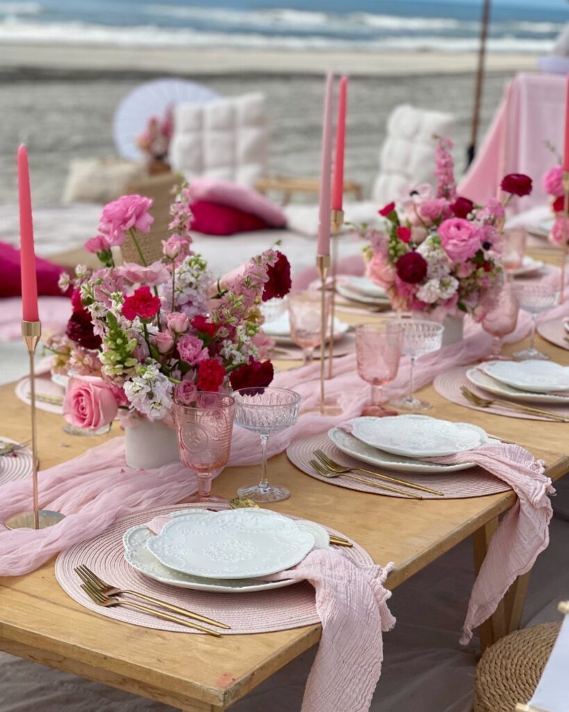 Pink floral table setting on a sandy beach with ocean waves in background