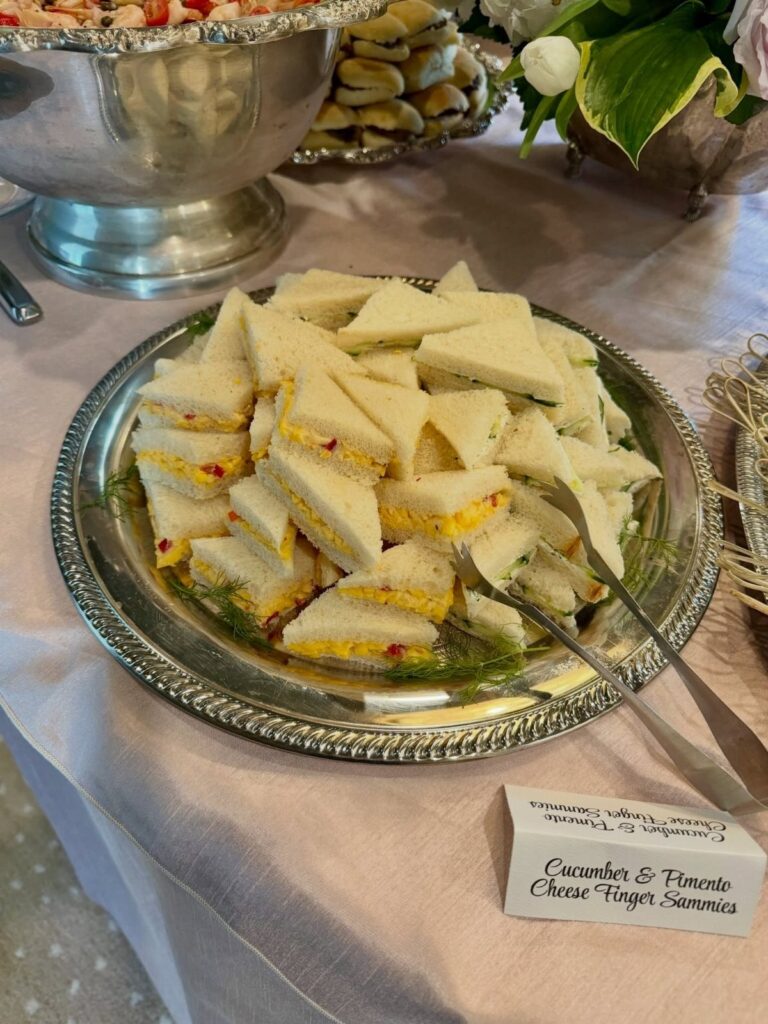 Triangular tea sandwiches on a silver platter with a descriptive food label.