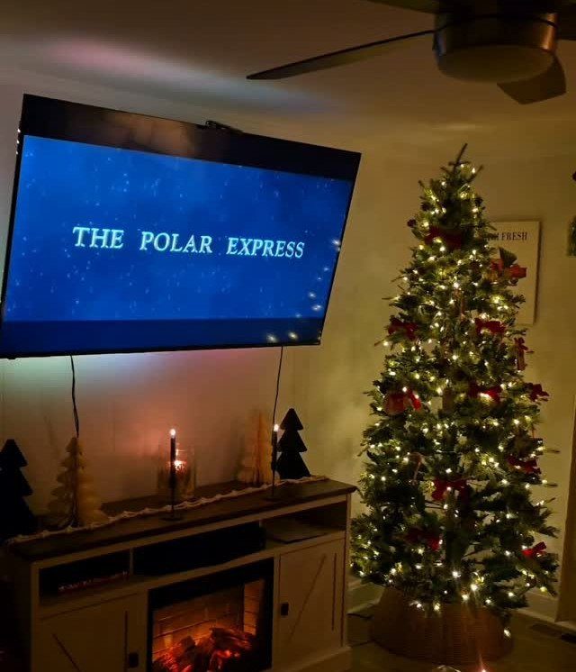 Television screen showing The Polar Express next to a decorated Christmas tree and fireplace.