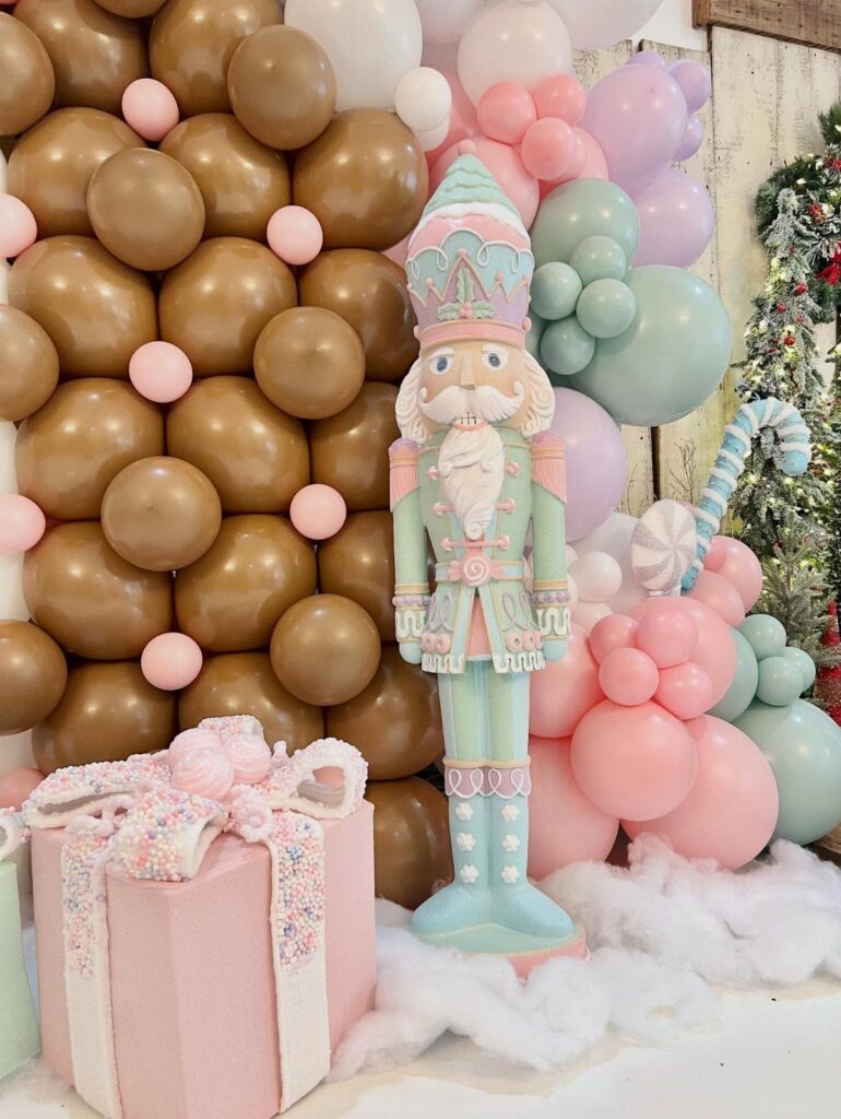 Mint green nutcracker statue with pink gift and pastel balloon wall decoration.
