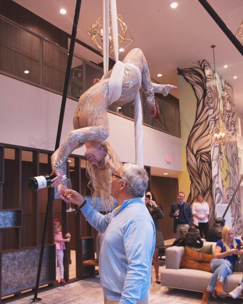 Aerial performer in gold bodysuit pouring champagne into a guest's glass from above.