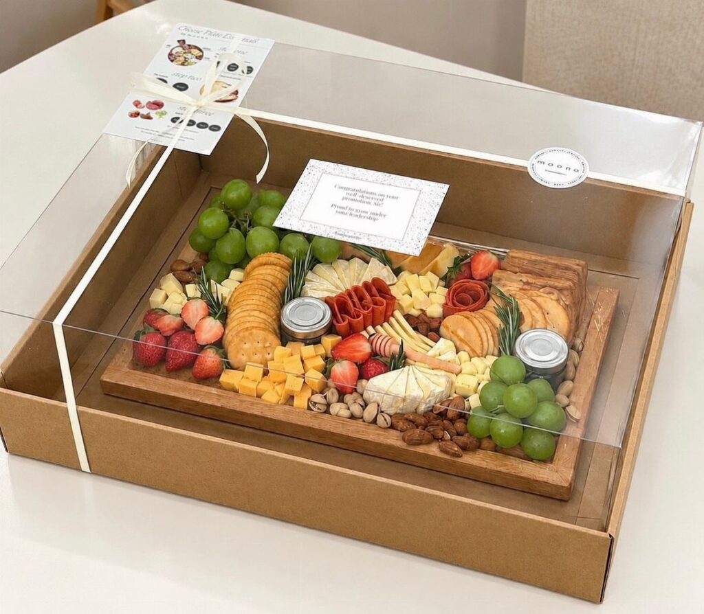 Charcuterie board gift box with grapes, cheese, and crackers under a clear lid