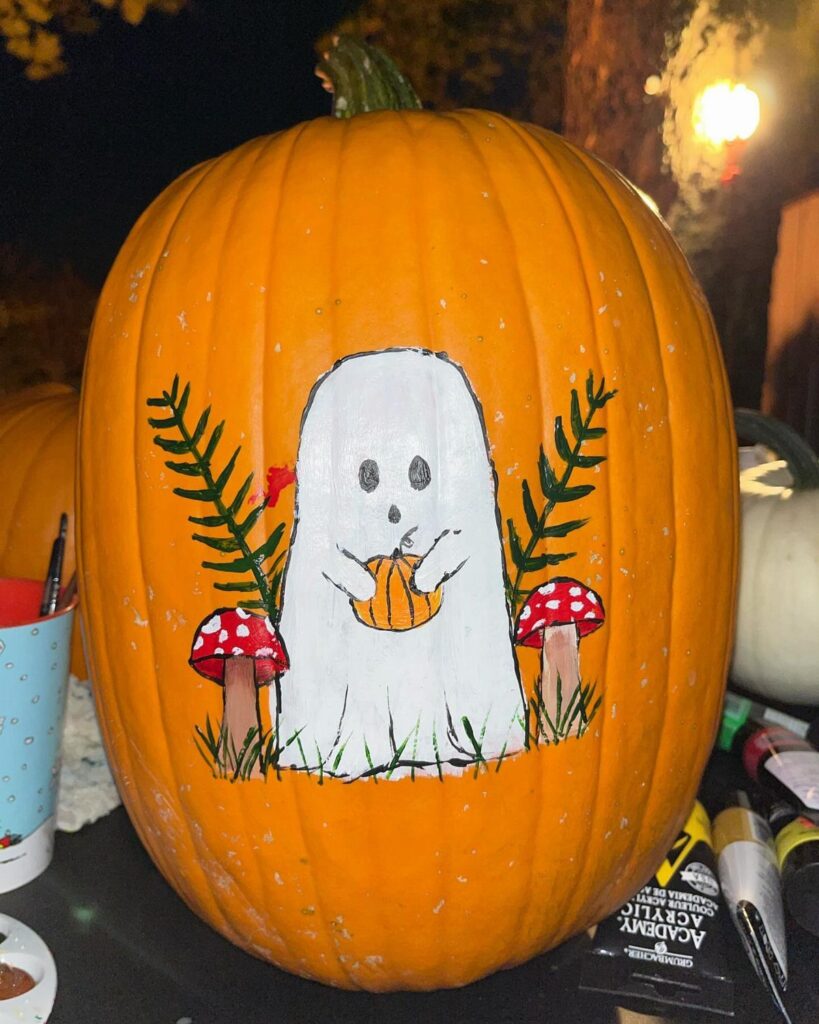 Orange pumpkin painted with a cute white ghost, red mushrooms, and green leaves.