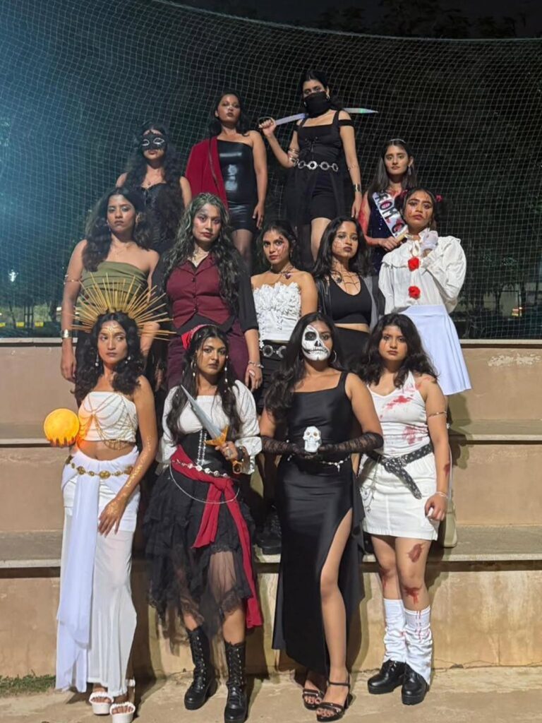 Group of women in diverse Halloween costumes posing on concrete steps at night.