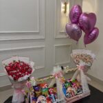 Two pink candy gift baskets with red roses and heart-shaped pink balloons.
