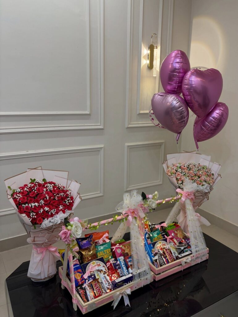 Two pink candy gift baskets with red roses and heart-shaped pink balloons.