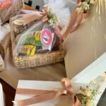 Wicker gift basket with snacks wrapped in cellophane and peach ribbons with flowers.