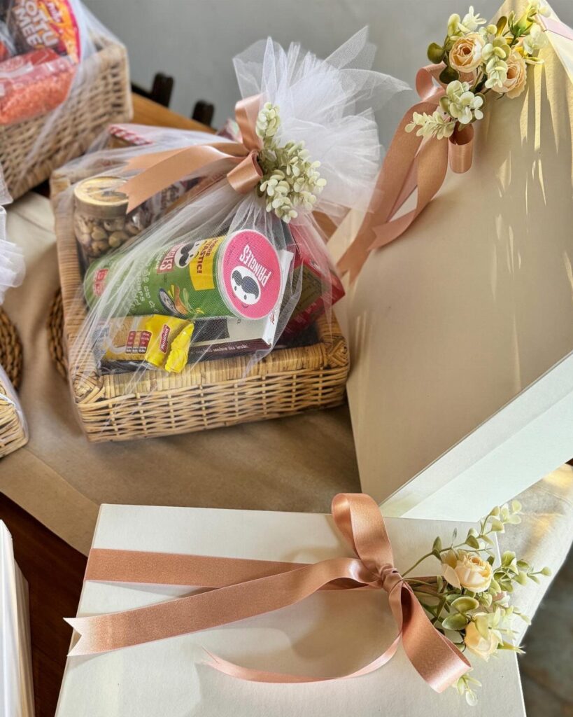 Wicker gift basket with snacks wrapped in cellophane and peach ribbons with flowers.