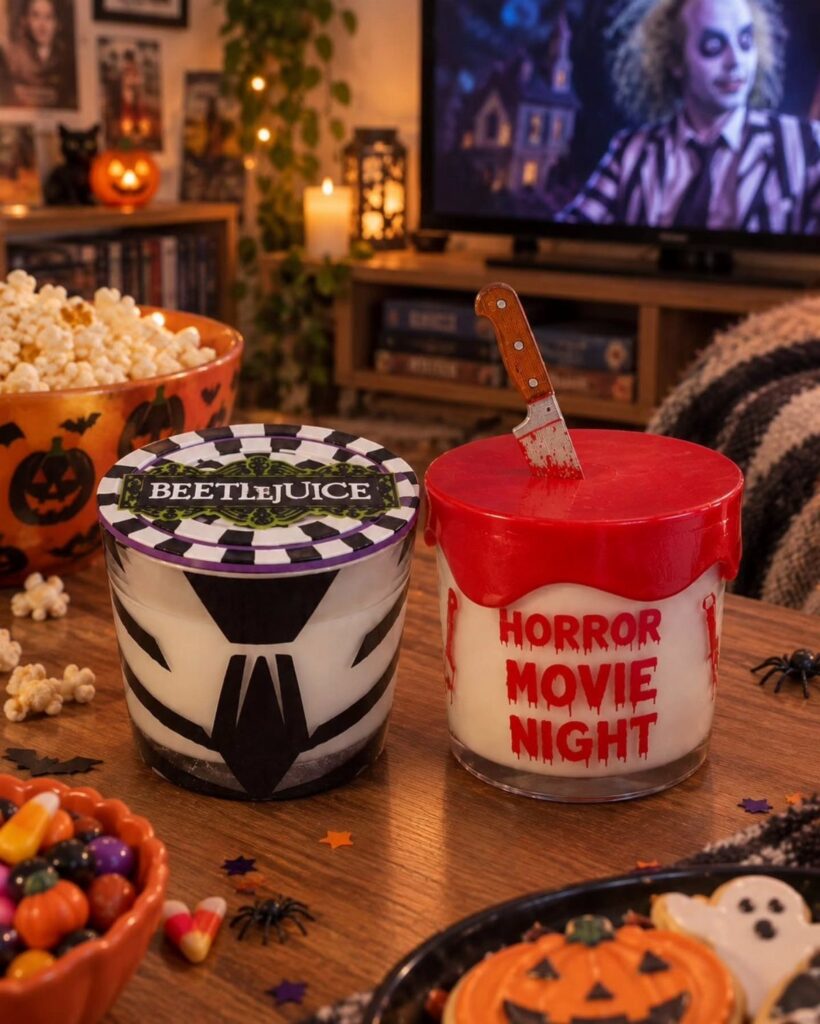 Themed Halloween candles on a table with popcorn and a movie playing behind.