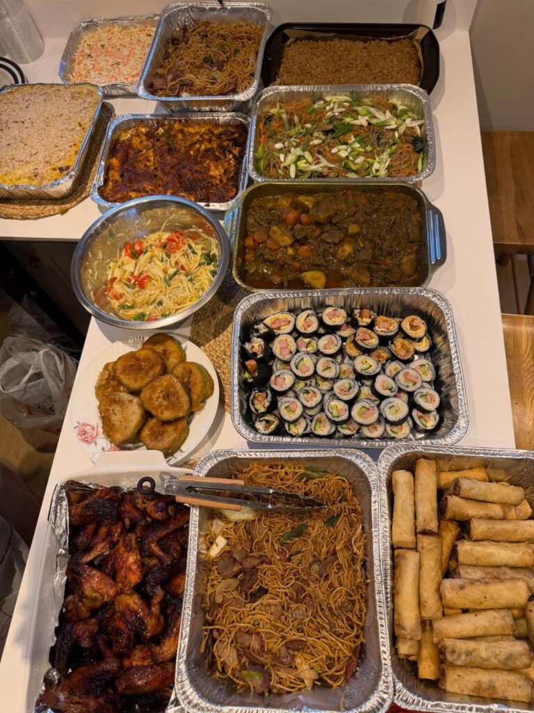 Assorted party foods in aluminum trays and bowls arranged on a white table.