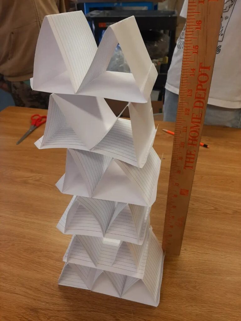 Folded white paper tower standing on a wooden table next to a yardstick.