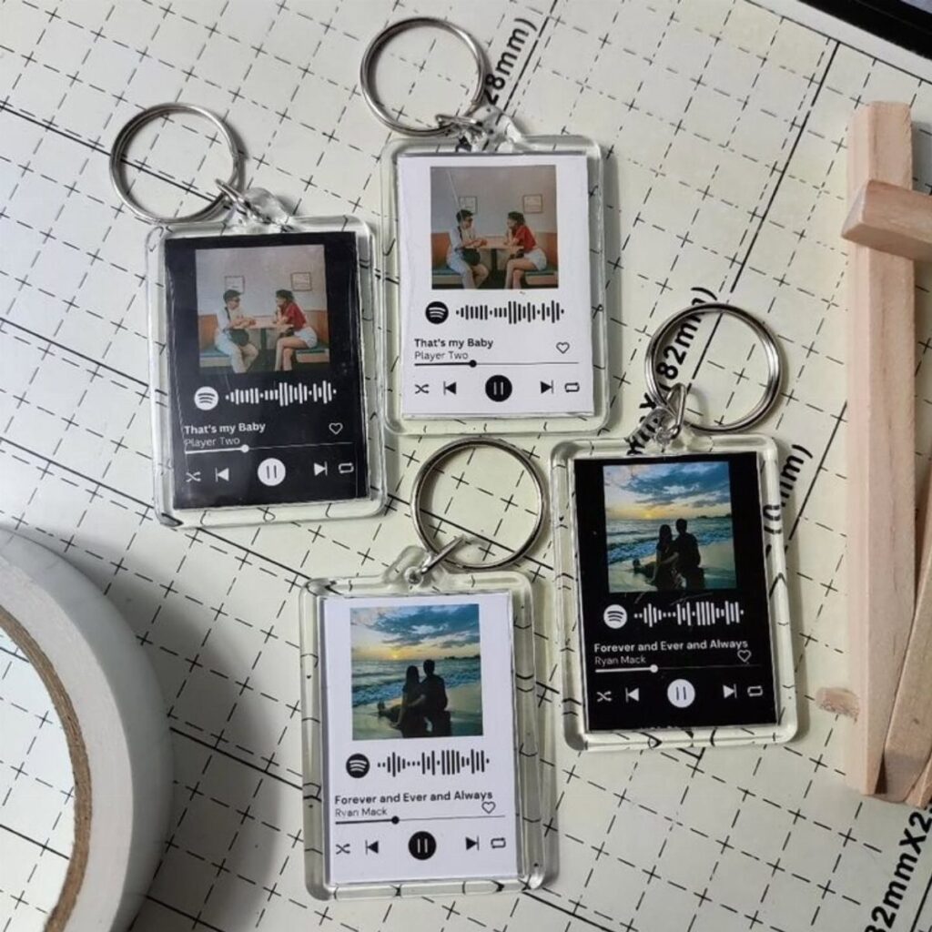 Four acrylic keychains featuring couple photos and music player interfaces on a grid mat.