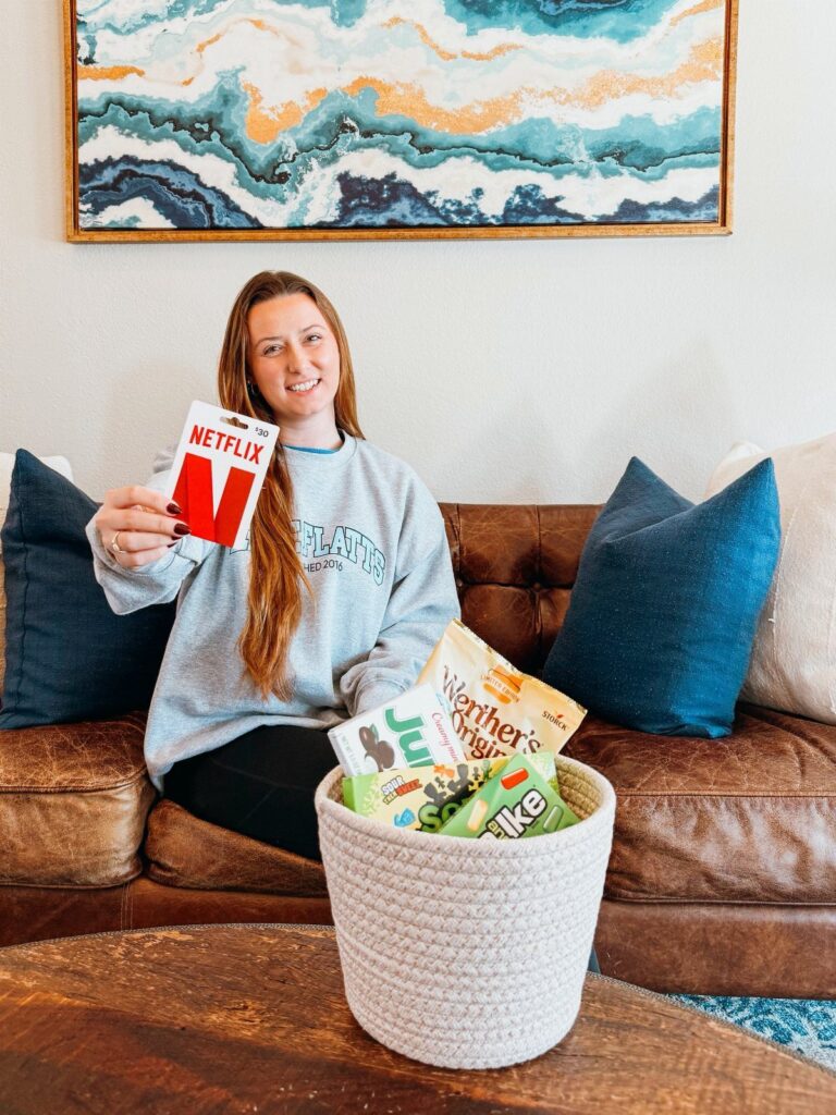Woman holding a Netflix gift card next to a snack-filled white woven basket.