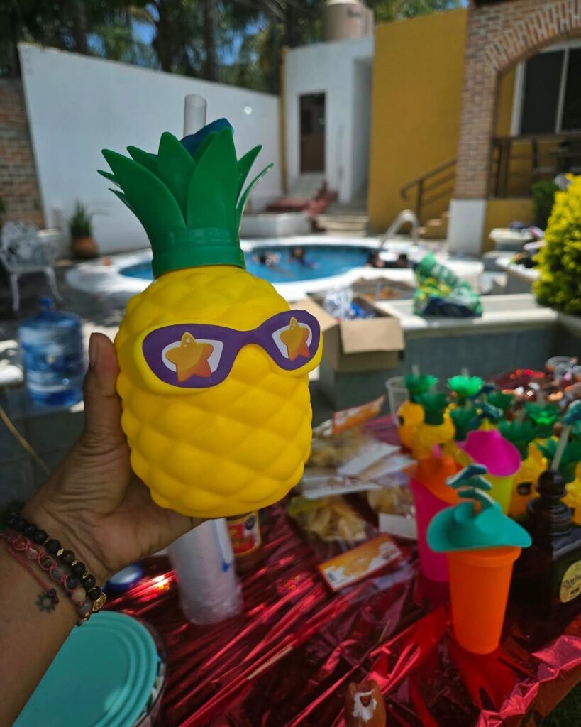 Pineapple shaped drink container with sunglasses held in front of a pool party