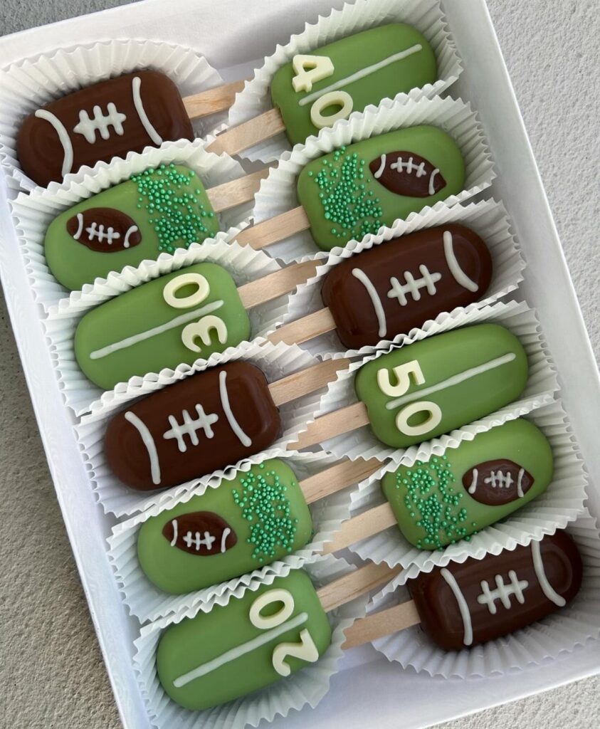 Football-themed cake pops in brown and green colors arranged in a white box.