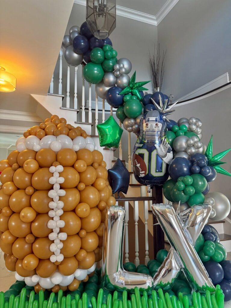 Football-shaped balloon sculpture and green, silver, and navy balloon arch on a staircase.