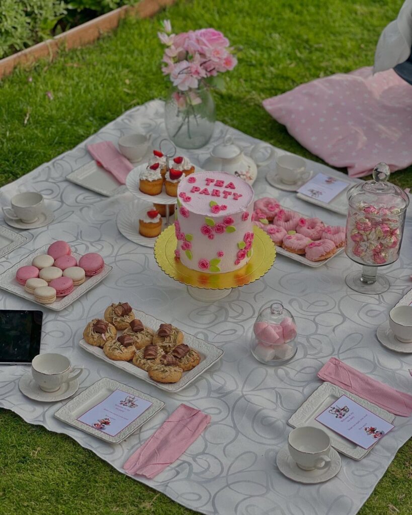 Tea party picnic spread with pink cake and sweets on a garden blanket