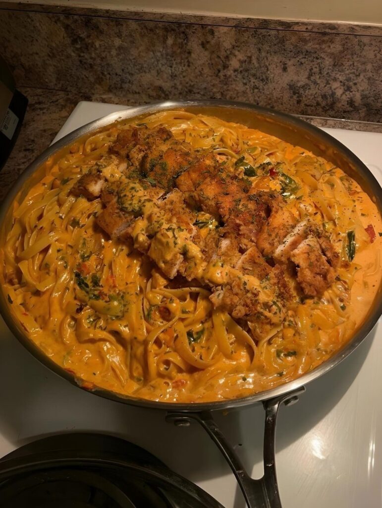 Breaded chicken breasts over creamy pasta in a stainless steel skillet